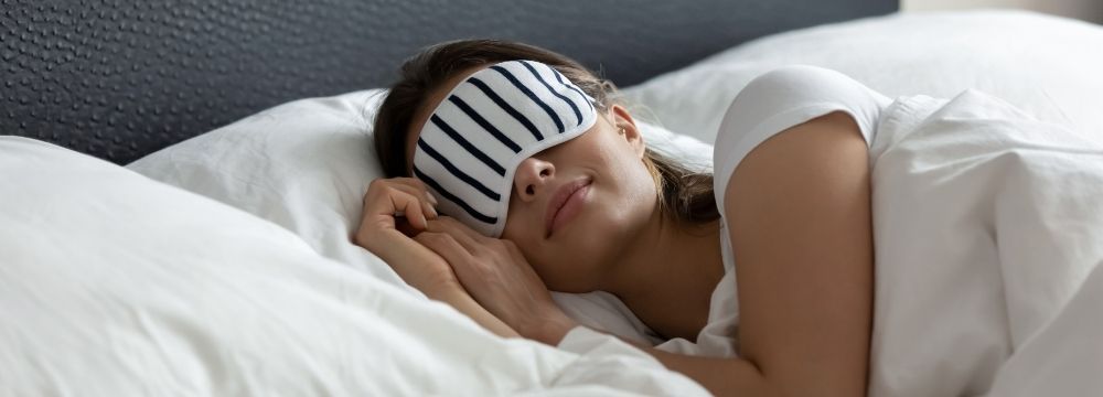 Woman sleeps soundly with eye mask on to ensure she gets adequate rest for her heart health per recommendations form Huntington Heart Center
