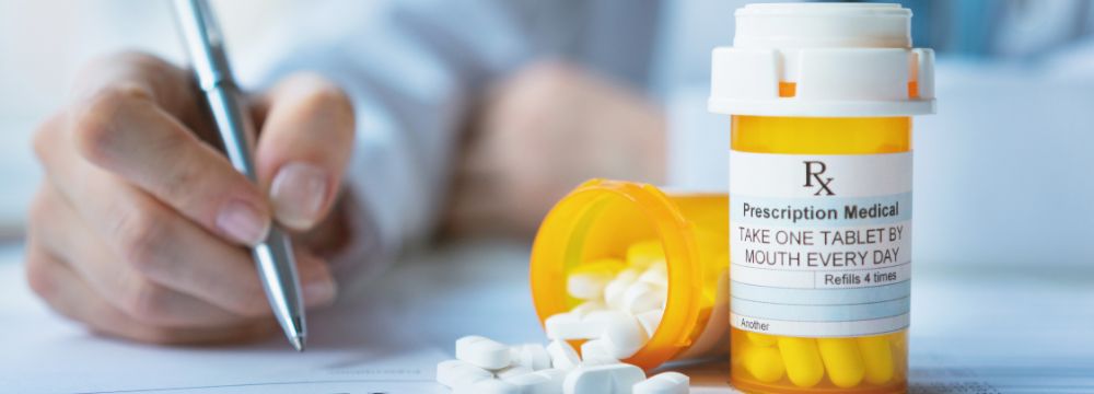 Doctor writing a prescription with pill bottles sitting on table